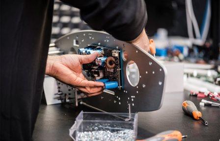 Technician fitting an amplifier board with blue capacitors to an aluminum chassis plate