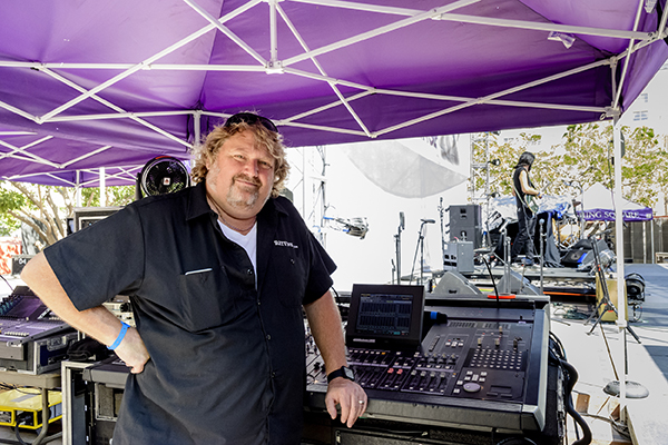 James Neal of CenterStaging at the mixing console under a purple tent, band on stage behind