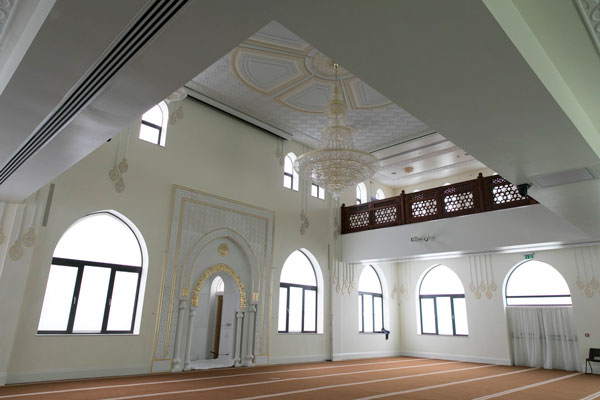 Prayer hall with a gilded mihrab, arched windows, a crystal chandelier and a wooden gallery
