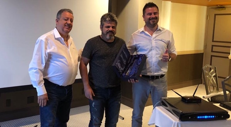 Three men at the distributors meeting; the man in the centre holds an award in a presentation case