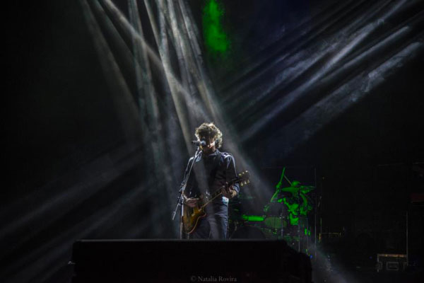 Cuarteto de Nos guitarist singing on stage under white light beams