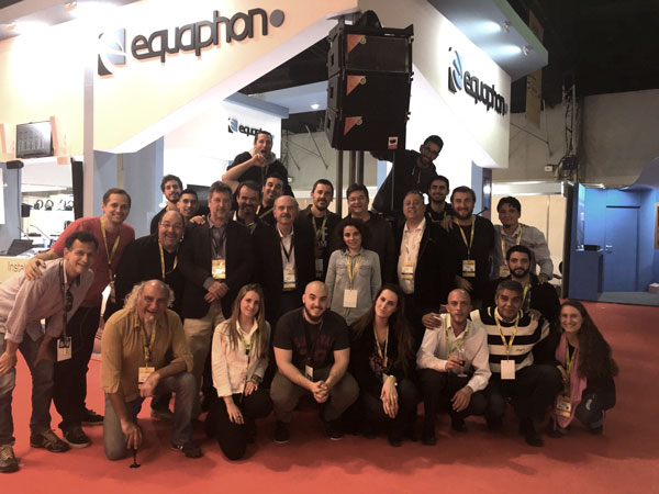 Group of people posing at the Equaphon stand at CAPER in Buenos Aires, under a hanging line array