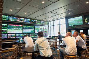 Sports bar with a wall of screens showing horse racing and patrons at high tables
