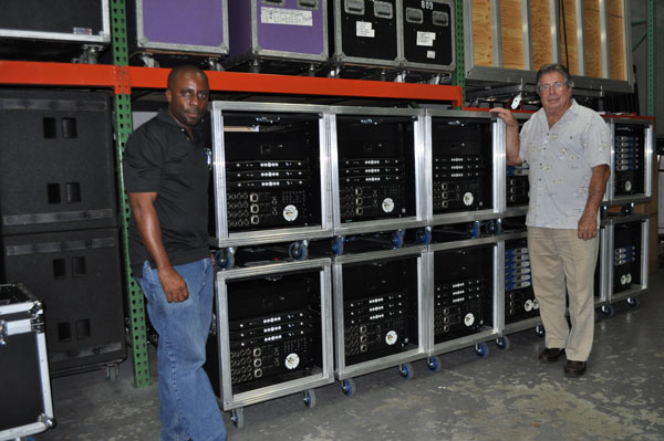 Two men beside stacked rack cases of Powersoft X4 amplifiers in a warehouse