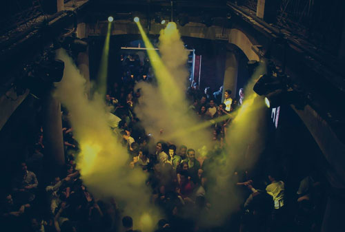 Crowd on the Grill dance floor under yellow light beams and haze