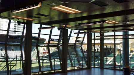Athletic club studio with ceiling lights and fans, and glass walls overlooking stadium stands