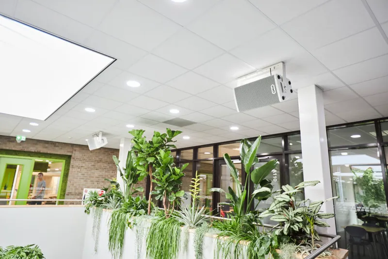 School atrium with indoor planters and a white loudspeaker mounted under the ceiling