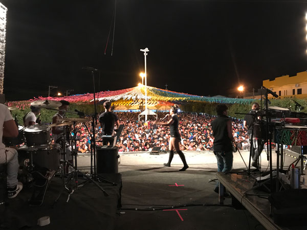 View from behind the band toward a large crowd at a night concert under colorful bunting