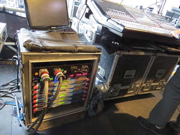 Rack of blue Powersoft K Series amplifiers next to a digital mixing console