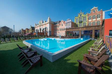 Outdoor pool at Plopsaqua with wooden deck chairs and colorful building facades