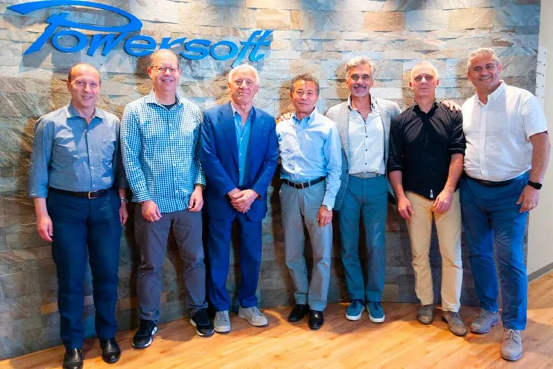 Seven men standing in front of a stone wall with the Powersoft logo