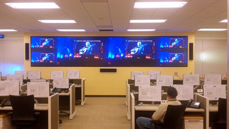 Security operations center with desk workstations and a video wall flanked by two loudspeakers