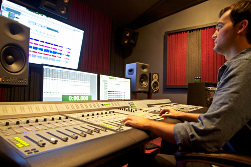 Engineer at a large mixing console in a studio, with monitor loudspeakers and screens