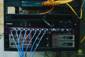 Rack with a network switch, a Furman power unit, a patch panel with blue cables and two Powersoft amplifiers