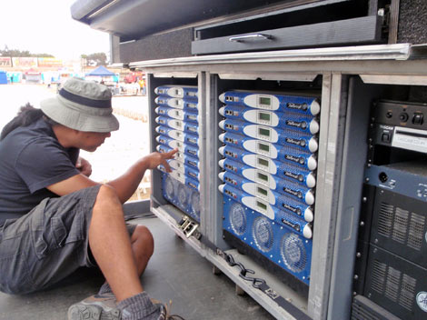 Technician pointing at two racks of Powersoft K3 amplifiers in an open equipment bay