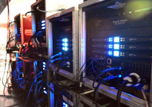 Row of touring amplifier racks with blue-lit front panels and cabling