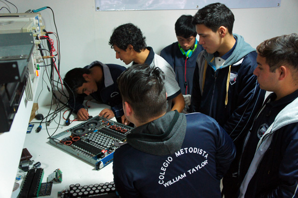 Colegio William Taylor students examining an amplifier circuit board at a workbench