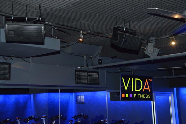 Diffusori montati sul soffitto di una sala cycling di VIDA Fitness illuminata di blu