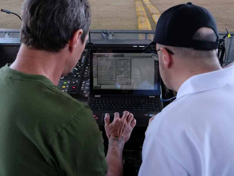 Two engineers seen from behind at a laptop and mixing console at an outdoor mix position