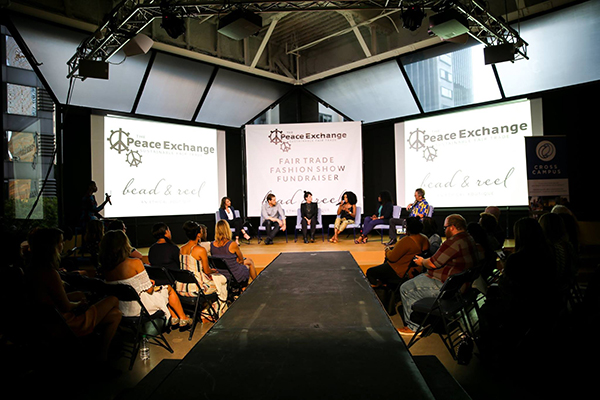 Panel on stage at a Fair Trade Fashion Show fundraiser at Cross Campus, audience along the runway