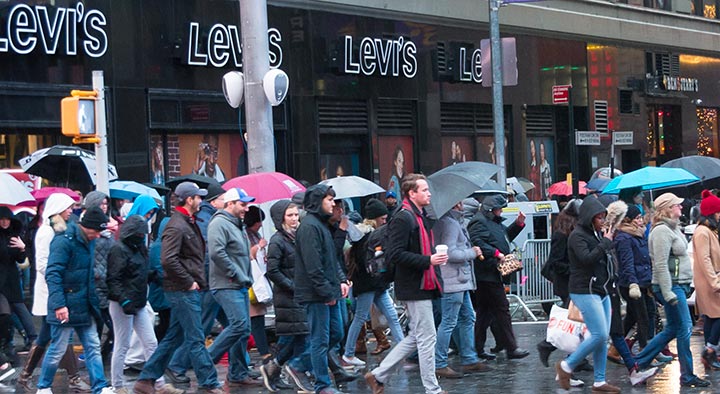 Pedestrians with umbrellas walk past two Deva units on a pole in Times Square