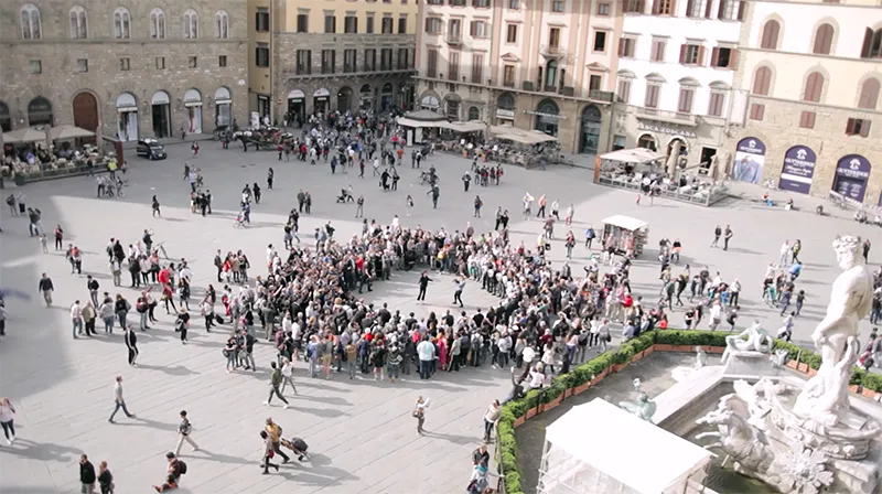 Aerial view of Piazza della Signoria in Florence, with a crowd standing in a circle next to the Neptune Fountain