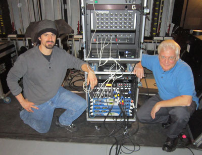 Two men beside a rolling rack with a Digico stage rack and Powersoft amplifiers