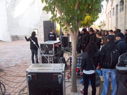 Outdoor demo with road cases and loudspeakers, watched by a group of people