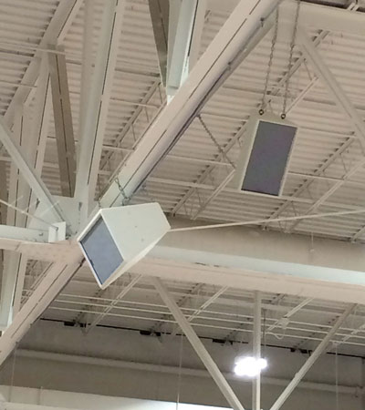 Two white loudspeakers hung from the roof trusses of a gymnasium