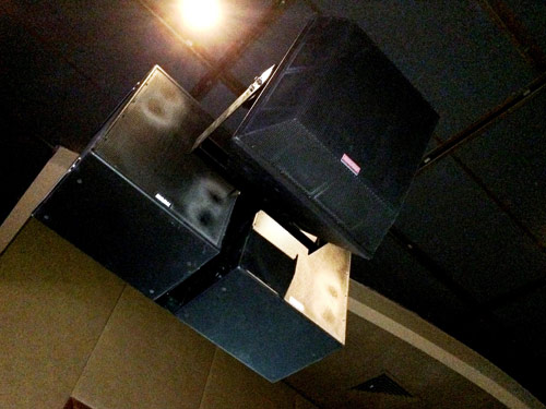 Cluster of three loudspeakers hung from the ceiling of the bar