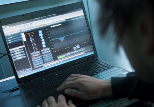 Hands on a laptop keyboard; the screen shows an equalizer curve in amplifier control software