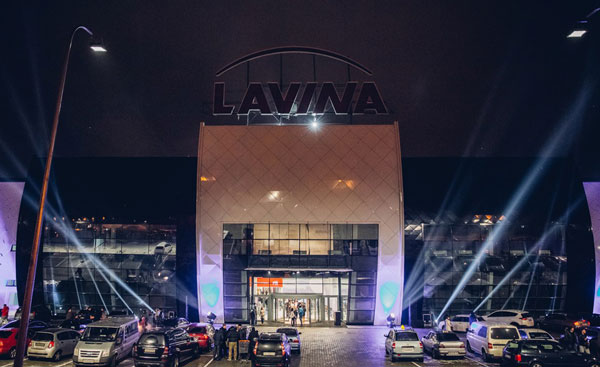 Lavina Mall entrance at night with searchlight beams and parked cars