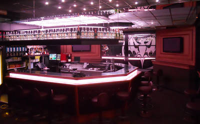 Bar counter lit in pink inside Club Reflex, with bottles on the back shelves