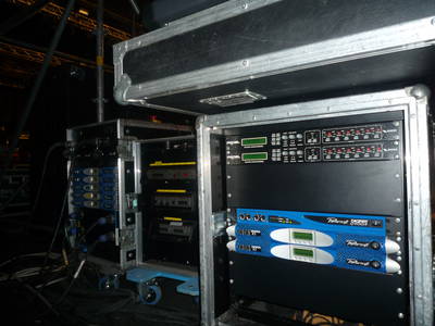 Rack in flight case dietro il palco con tre amplificatori Powersoft, fra cui un Q4004 e un K3, sotto due processori
