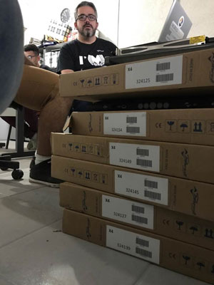 Six boxed Powersoft X4 amplifiers stacked on the floor, with staff seated behind