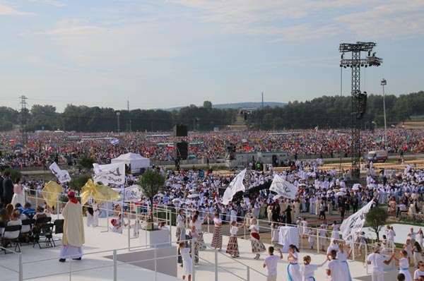 Clergy, flag bearers and dancers before a crowd of pilgrims at World Youth Day in Kraków, with a delay tower