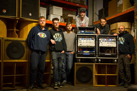 Mungo's Hi Fi crew with two amplifier racks and wooden speaker cabinets in a warehouse