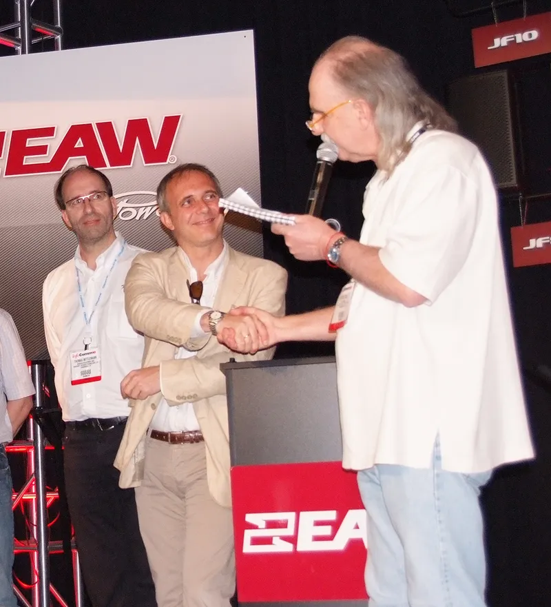 Handshake on stage at an EAW press conference at InfoComm 2010, in front of EAW and Powersoft logos