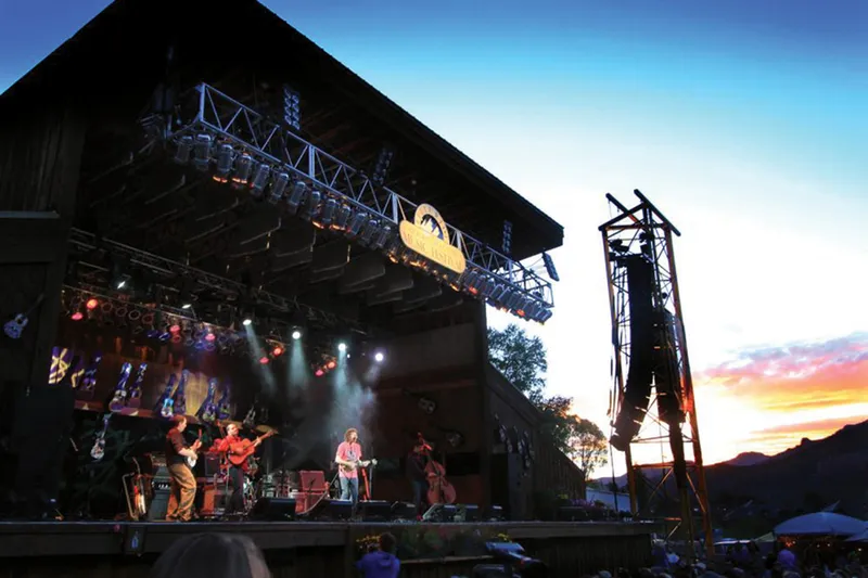 Band playing on the Telluride Bluegrass Festival stage at sunset, with a loudspeaker array hung from a side tower