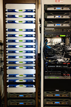 Rack of Powersoft K2 amplifiers beside a second rack with network cabling and an Allen & Heath iDR-64