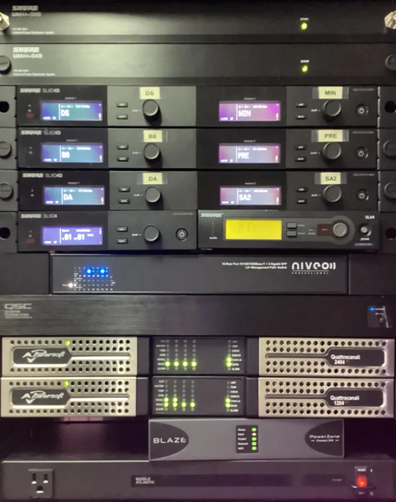Rack with Shure wireless receivers, a network switch and Quattrocanali 2404 and 1204 amplifiers