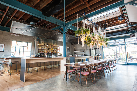 Rose Cafe dining room with a long table, bar counter and hanging plants under a wooden roof