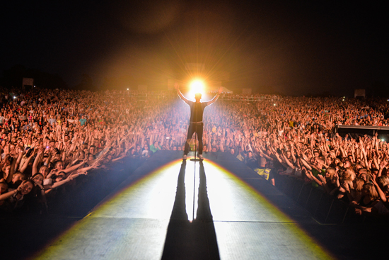 Sel on stage with arms raised, backlit, facing a large crowd at night