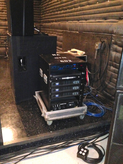 Rolling equipment rack next to loudspeaker cabinets in a rehearsal room with padded walls