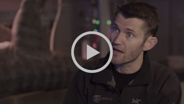Play button over a video interview with a man wearing an Auditoria jacket