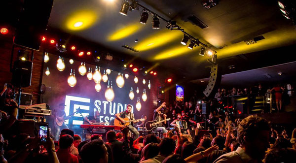 Acoustic band performing at Woods SP nightclub, with a hanging line array and bulb lights above the crowd