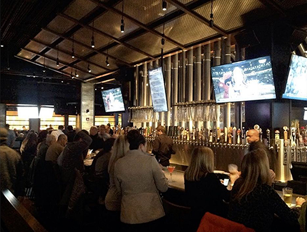 Yard House bar with rows of beer taps, TV screens and customers at the counter